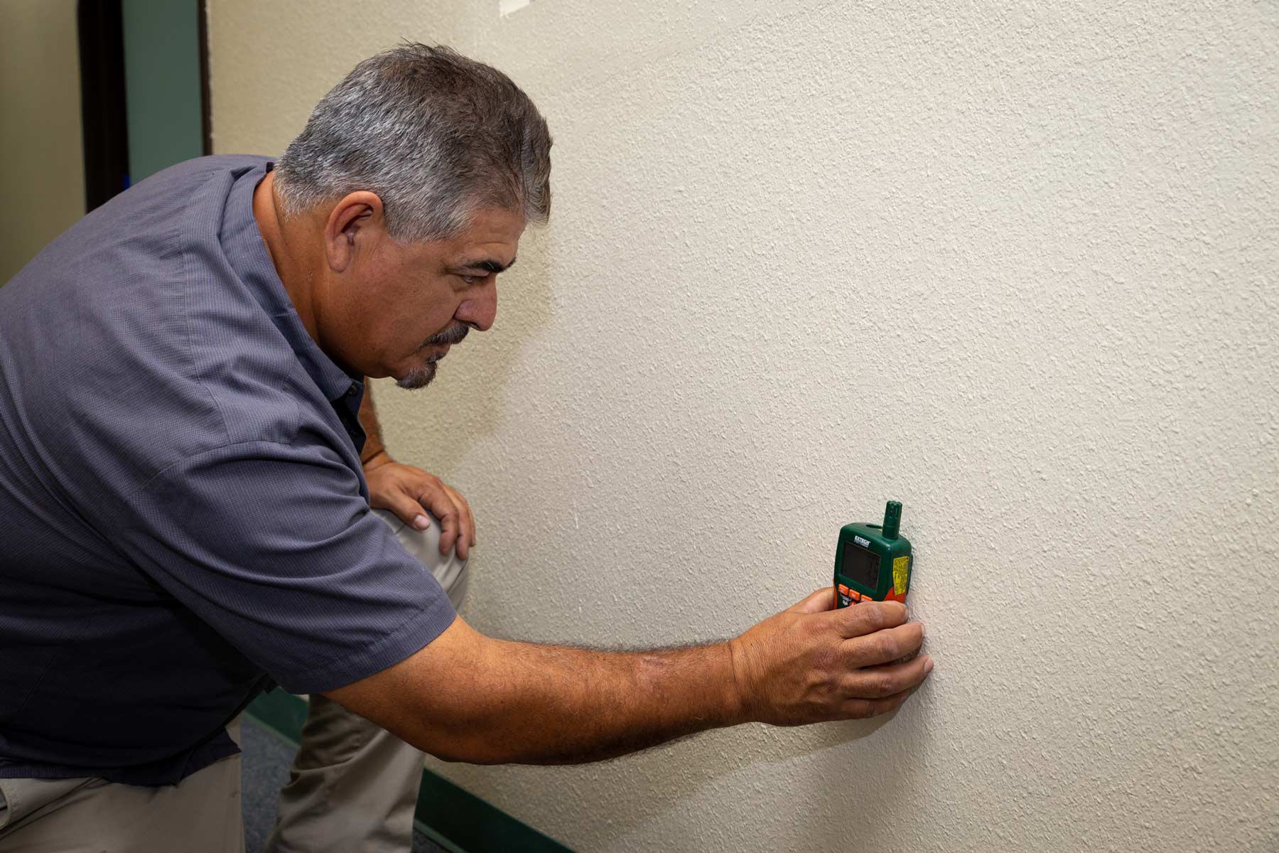 Experienced water damage restoration technician testing wall for moisture
